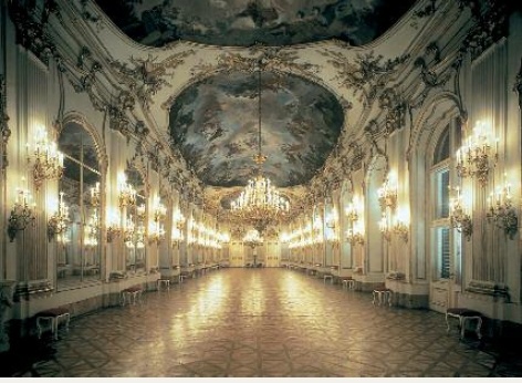 シェーンブルン宮殿の公式行事用ホールは、左右両側の壁が多数の燭台で明るく照らされ、その天井には豪華な天井画が描かれています。